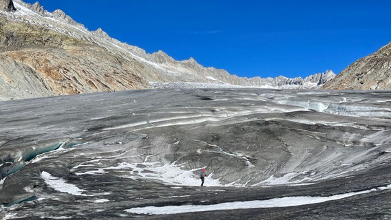 Eine Gletscherabsenkung aufgrund eines unterirdischen Gletscherbaches, daneben eine Person. © ARD Foto: Kathrin Hondl