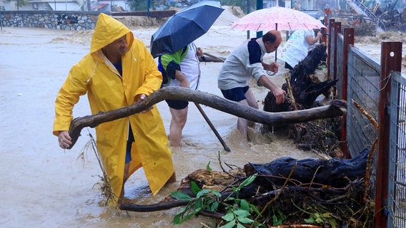 Personen mit Regenschirmen, im Wasser stehend, entfernen Trümmer an einem Zaun (Mittelgriechenland). © dpa bildfunk Foto: George Kidonash