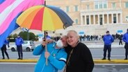 Zwei Frauen in Athen halten einen Regenschirm in Regenbogenfarben über sich © picture alliance / Sipa USA | Kostas Galanis Foto: Kostas Galanis