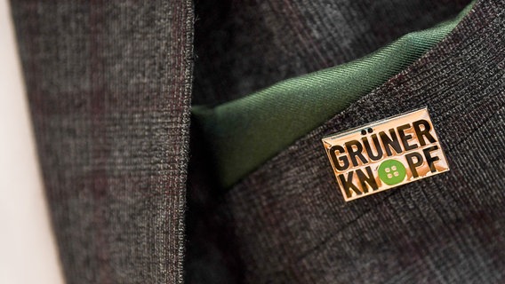 Ein Anstecker mit dem Symbol des staatlichen Textilsiegels "Grüner Knopf" am Revers eines Anzug-Jacketts. © dpa picture alliance Foto: Britta Pedersen