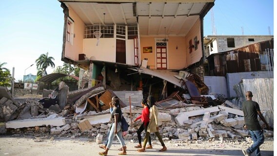 Menschen gehen an einem durch das Erdbeben zerstörten Haus in Les Cayes, Haiti, vorbei. © dpa-Bildfunk Foto: Joseph Odelyn