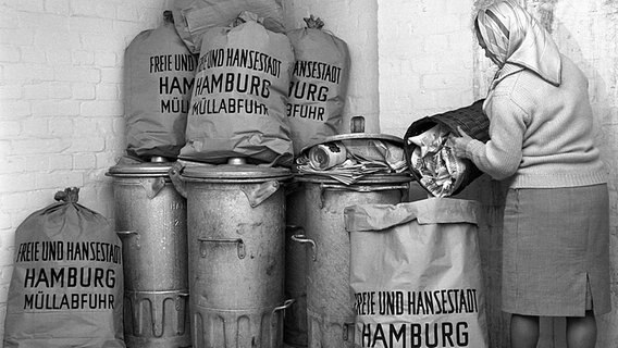 Frau mit Kopftuch schüttet Abfall in einen Sack mit Aufschrift "Freie und Hansestadt Hamburg Müllabfuhr" (1963). © picture alliance Foto: Lothar Heidtmann