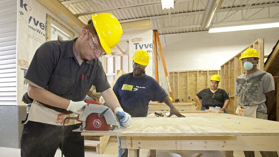 Ein Ausbilder beobachtet einen Lehrling bei der Arbeit mit der Kreissäge. Ein Ausbilder beobachtet einen Lehrling bei der Arbeit mit der Kreissäge. © picture alliance/imageBROKER Foto: Jim West