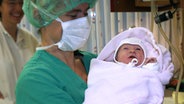 Eine Hebamme in OP Kleidung hält ein Neugeborenes auf dem Arm. © picture-alliance/ dpa Foto: Marcus Führer