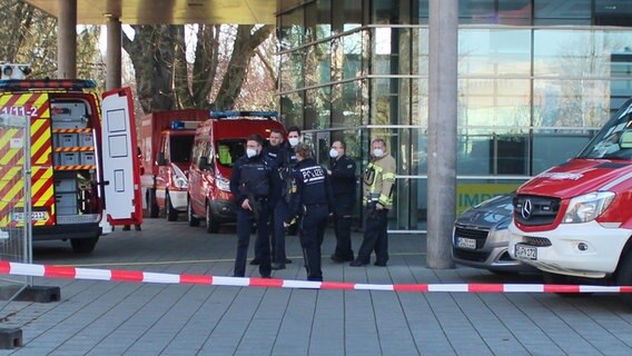 Polizisten stehen neben Krankenwagen und Fahrzeugen der Feuerwehr auf dem Gelände der Heidelberger Universität an einem Eingang zu einer Klinik, die sich auf dem Campus befindet. © R.Priebe//Pr-Video/dpa 