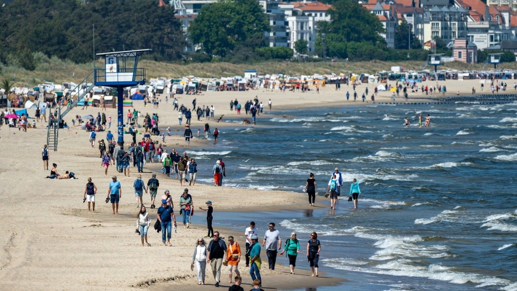Spaziergänger sind bei sonnigem Wetter am Strand von Heringsdorf auf der Insel Usedom unterwegs