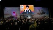 Sayyed Hassan Nasrallah, Hisbollah-Führer, grüßt seine Anhänger während einer Videoübertragung im Rahmen einer Zeremonie zum vierten Jahrestag der Ermordung des iranischen Quds-Truppengenerals Soleimani. © Hassan Ammar/AP/dpa 
