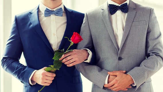 Zwei Männer im Anzug stehen eingehakt mit einer Rose in der Hand. © fotolia Foto: SydaProductions