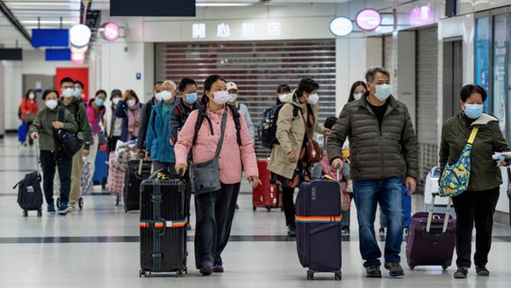 Reisende mit Mund-Nasen-Schutz gehen mit ihrem Gepäck zum Schalter in der Halle des Hongkonger Bahnhofs Lok Ma Chau, nachdem der Grenzübergang zum chinesischen Festland wieder geöffnet wurde. © Bertha Wang/AP/dpa 