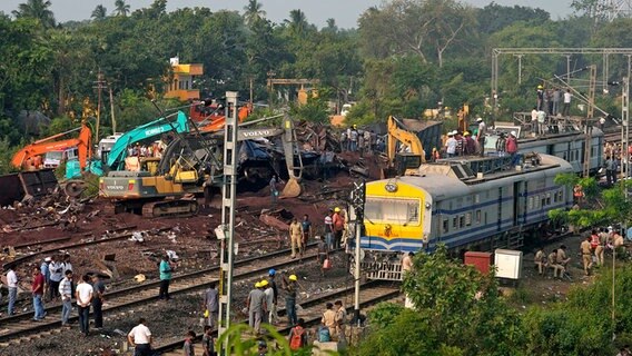 Menschen beobachten die Stelle, an der die Züge im Bezirk Balasore im ostindischen Bundesstaat Orissa entgleist sind. © dpa-Bildfunk/AP Foto: Rafiq Maqbool