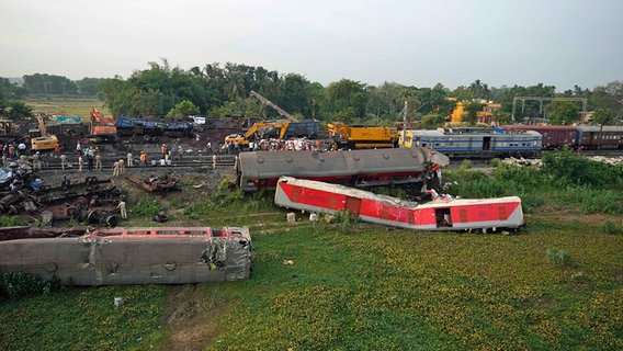 Menschen beobachten die Stelle, an der die Züge im Bezirk Balasore im ostindischen Bundesstaat Orissa entgleist sind. © dpa-Bildfunk/AP Foto: Rafiq Maqbool