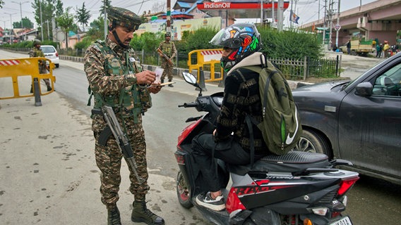 Ein indischer paramilitärischer Soldat kontrolliert den Ausweis eines Rollerfahrers an einem provisorischen Kontrollpunkt auf der Straße zum Flughafen in Srinagar, im indisch kontrollierten Kaschmir. © Dar Yasin/AP/dpa 
