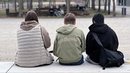 Drei Jugendliche sitzen in München in einem Park nebeneinander. © picture alliance / SvenSimon | FrankHoermann 