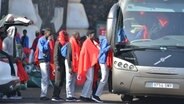 Einige der Migranten, die mit einem Boot auf der Insel El Hierro angekommen sind, besteigen einen Bus. © Europa Press/EUROPA PRESS/dpa 