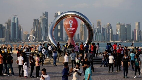 Menschen versammeln sich um die offizielle Countdown-Uhr, die die verbleibende Zeit bis zum Anpfiff der Fußballweltmeisterschaft 2022 anzeigt. © Hassan Ammar/AP/dpa 