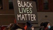 Ein Demonstrant hält ein Schild mit der Aufschrift "Black Lives Matter" während eines Protestmarsches in Brooklyn gegen den Freispruch von Kyle R. hoch. © dpa-Bildfunk 