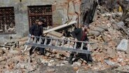 Zwei Männer tragen während der Aufräumarbeiten nach einem Raketenangriff in Kiew eine Leiter an einem zerstörten Haus vorbei. ©  -/Ukrinform/dpa 