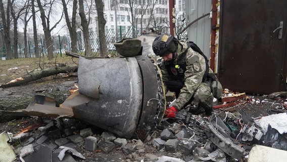 Ein ukrainischer Polizist inspiziert ein Raketenteil in der Nähe eines durch einen russischen Raketeneinschlag beschädigten Wohnhauses. © Andrii Marienko/AP/dpa 