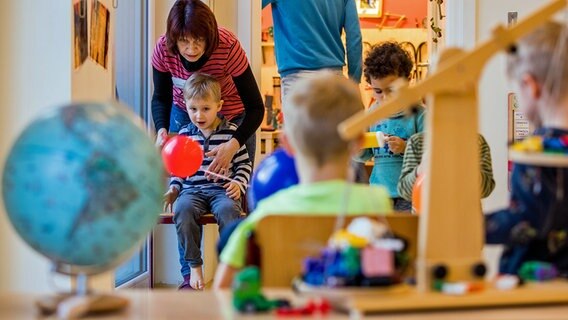 Mehrere Kinder spielen in einer Kita. Im Hintergrund ist eine Erzieherin zu sehen. © dpa picture alliance Foto: Jens Büttner