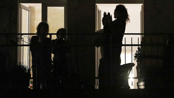 Menschen stehen im Dunkeln auf einem Balkon und klatschen. © dpa bildfunk Foto: Oliver Berg