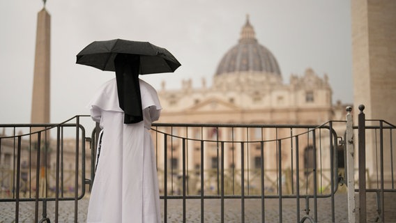 Eine Nonne schützt sich vor dem Regen, während sie die letzte Messe der Kardinäle im Petersdom vor dem Konklave zur Wahl eines neuen Papstes auf dem Petersplatz verfolgt. © Francisco Seco/AP/dpa Foto: Francisco Seco