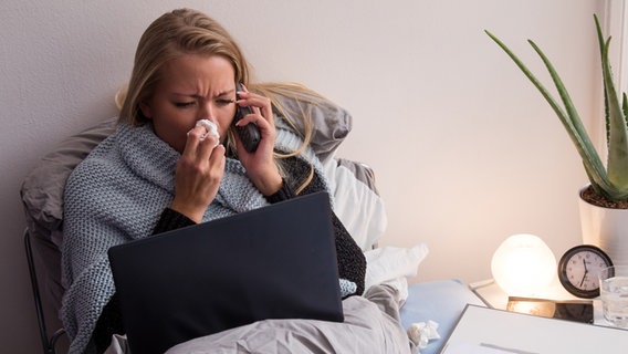 Eine Frau liegt in einer Wohnung krank im Bett und putzt sich die Nase. © picture alliance / Christin Klose 
