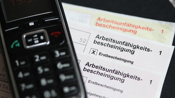 Ein Telefon liegt auf einer Arbeitsunfähigkeitsbescheinigung. © picture alliance / Eibner-Pressefoto 