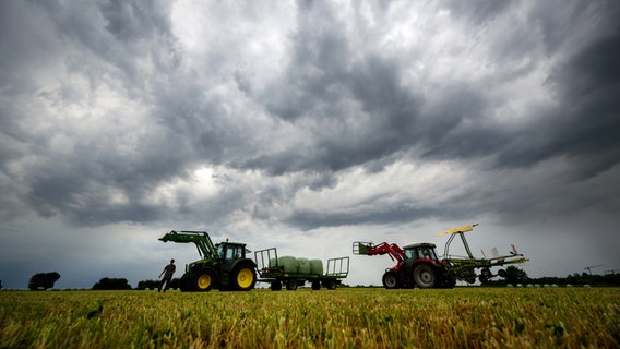 Landwirte in Niedersachsen verladen Heuballen, während am Himmel eine Gewitterfront aufzieht. © picture alliance/dpa | Julian Stratenschulte 