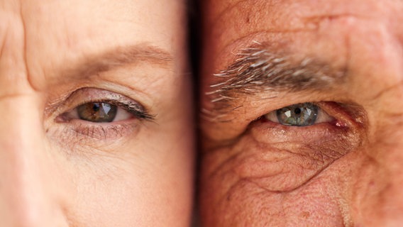 Ein Mann und eine Frau blicken mit den Gesichtern dicht beieinander in die Kamera. Zu sehen ist nur jeweils ein Auge, die Frau hat weniger, der Mann mehr Falten. © colourbox / Peopleimages.com 