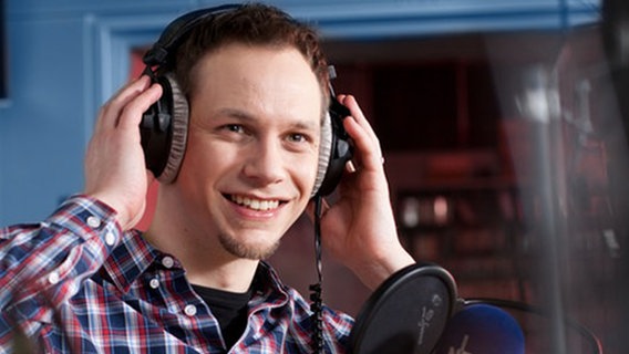Michael Latz steht in einem Studio vor einem Mikrofon und hat Kopfhörer auf. © NDR 