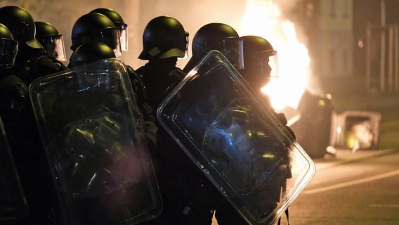 Polizisten stehen in Leipzig in Schutzausrüstung an einem brennenden Müllcontainer. © dpa-Bildfunk Foto: Sebastian Willnow