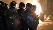 Polizisten stehen in Leipzig in Schutzausrüstung an einem brennenden Müllcontainer. © dpa-Bildfunk Foto: Sebastian Willnow