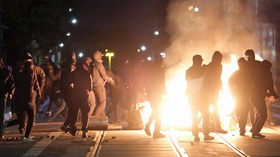 Mehrere Menschen stehen im Dunklen vor einer brennenden Barrikade auf einer Straße. © dpa-Bildfunk Foto: Sebastian Willnow