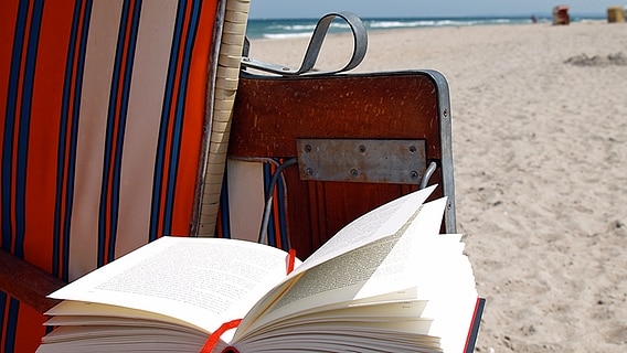 Ein aufgeschlagenes Buch liegt in einem Strandkorb am Strand. Ein aufgeschlagenes Buch liegt in einem Strandkorb am Strand. © NDR/Katharina Mahrenholtz Foto: Katharina Mahrenholtz