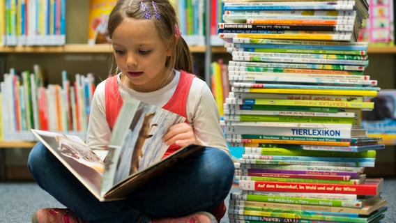 Ein Mädchen sitzt in einer Bibliothek vor vielen Kinderbüchern © picture-alliance / dpa 