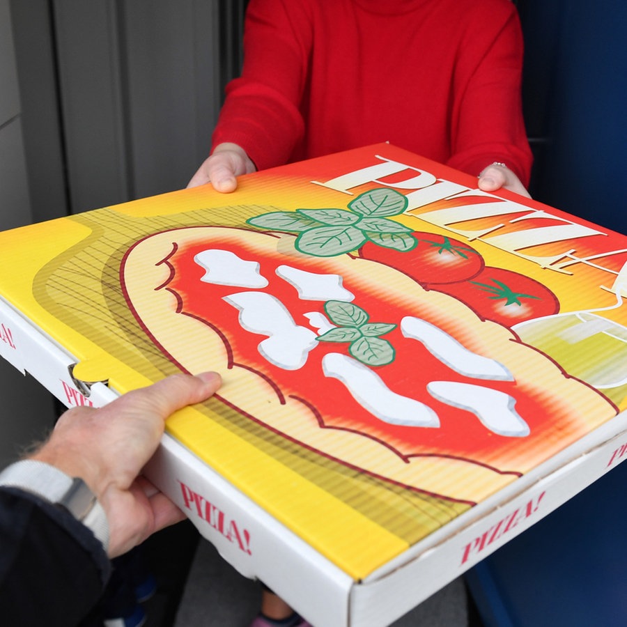 Eine Pizzaschachtel wird an der Haustür von einem Lieferdienst an eine Kundin übergeben © picture alliance / SvenSimon Foto: FrankHoermann/SVEN SIMON