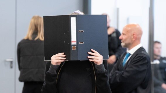 Dresden: Die Angeklagte Lina E. steht bei der Fortsetzung des Prozesses im Oberlandesgericht (OLG) Dresden im Verhandlungssaal und hält einen Aktenordner vor ihr Gesicht. © dpa Foto: Sebastian Kahnert/