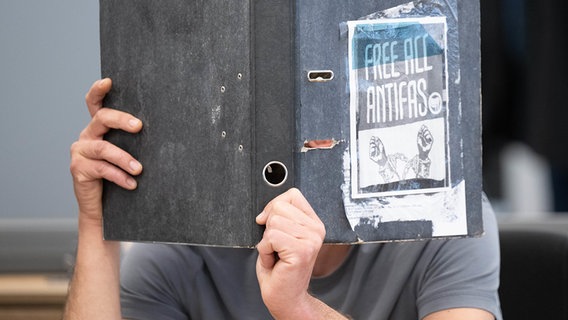 A woman covers her face with a file folder.  © dpa Bildfunk 