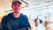 Luca, Student in Hamburg, sitzt in der Pizzeria auf dem Campus in Hamburg und blickt in die Kamera. © NDR Info Foto: Lisa Hentschel
