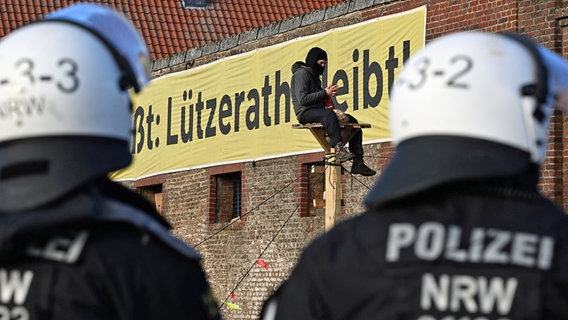 Ein Demonstrant sitzt bei der Räumung des Dorfes Lützerath auf einer Holzkonstruktion vor einem Plakat mit dem Slogan "Lützerath bleibt!". © dpa bildfunk Foto: Federico Gambarini