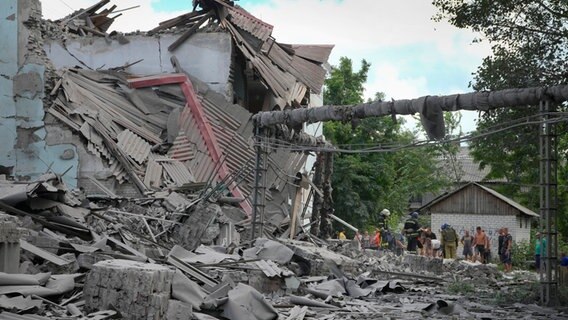 Rettungskräfte und Anwohner stehen nach einem russischen Luftangriff bei den Trümmern eines Gebäudes in Lyssytschansk © Efrem Lukatsky/AP/dpa 