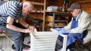 Zwei Männer arbeiten in einer Werkstatt an einem Holzmöbelstück. © NDR Foto: Eva Werler