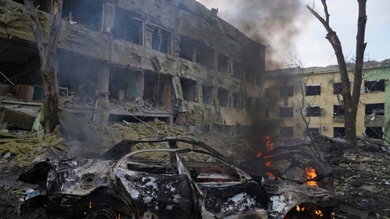 Ein Auto brennt neben einer durch einen Angriff beschädigten Geburtsklinik in Mariupol. © dpa-Bildfunk Foto: Foto: Evgeniy Maloletka/AP/dpa