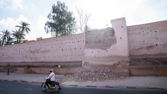 Marokko, Marrakesch: Ein Mann fährt nach einem Erdbeben mit seinem Auto an einer beschädigten Mauer in der historischen Stadt vorbei.  © Musaab Al-Shami/AP/DPA 
