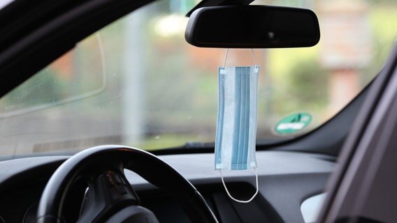 Eine blaue Einwegschutzmaske hängt an einem Rueckspiegel im Innenraum eines Autos. © picture alliance / Eibner-Pressefoto Foto: Fleig / Eibner-Pressefoto