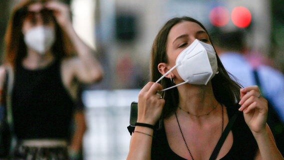 Eine Frau nimmt in einer Einkaufsstraße ihre Mund-Nasen-Bedeckung ab. © picture alliance/dpa/LaPresse via ZUMA Press Foto: Cecilia Fabiano