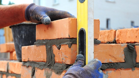 Maurer hält eine Wasserwaage gegen frisch zementierte Mauer. © Fotolia.com Foto: bildlove