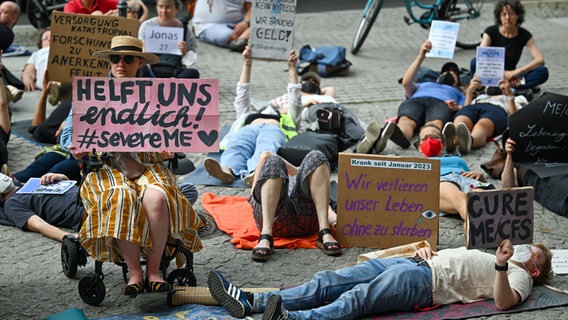 Demonstranten mit unter anderem dem Schild "Wir verlieren unser Leben, ohne zu sterben" haben sich vor dem Roten Rathaus für fünf Minuten zu einer Liegend-Demo auf den Boden gelegt. Die "Rollstuhldemo für die Inklusion und Sichtbarkeit von Menschen mit ME/CFS" wollte so auf die neuroimmunologische Krankheit Myalgische Enzephalomyelitis /Chronisches Fatigue Syndrom (ME/CFS) aufmerksam machen, die zu einem hohen Grad an der körperlichen Behinderung führen kann. (Foto vom 8.8.2024) © picture alliance/dpa | Soeren Stache 