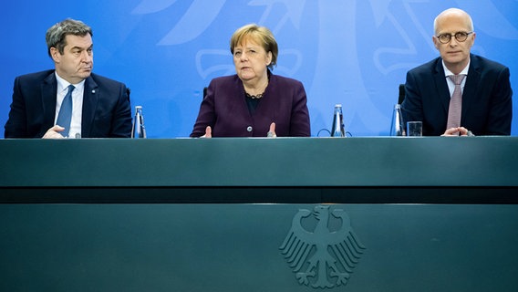 Die Politiker Markus Söder (CSU), Angela Merkel (CDU) und Peter Tschentscher (SPD) sitzen bei einer Pressekonferenz nebeinander auf einem Podium. © dpa bildfunk Foto: Bernd von Jutrczenka