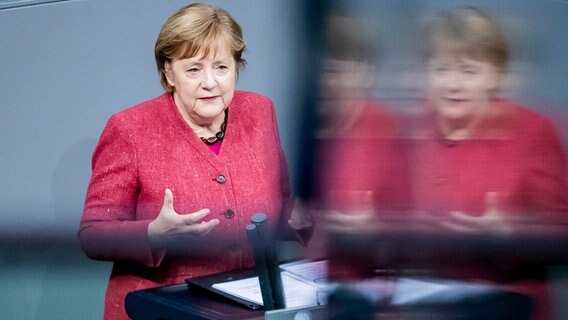 Bundeskanzlerin Angela Merkel (CDU) spricht während einer Generaldebatte zum Bundeshaushalt im Bundestag, wobei sich ihr Bild auf einer Scheibe spiegelt. © dpa Foto: Christoph Soeder